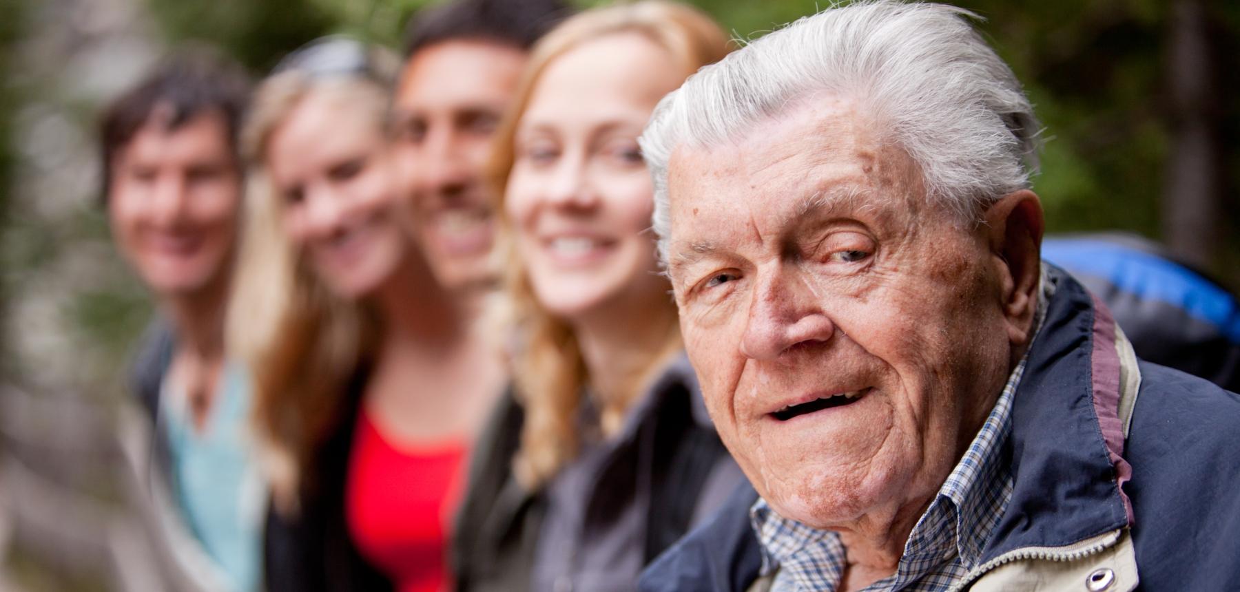 Äldre man och i bakgrunden andra personer i varierande åldrar.